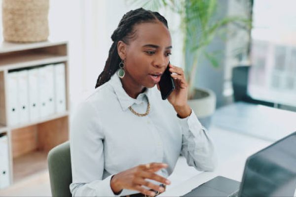 Business woman, phone call and laptop for online research in office and talking of information on website. Black person, government or professional with smartphone or discussion on public governance